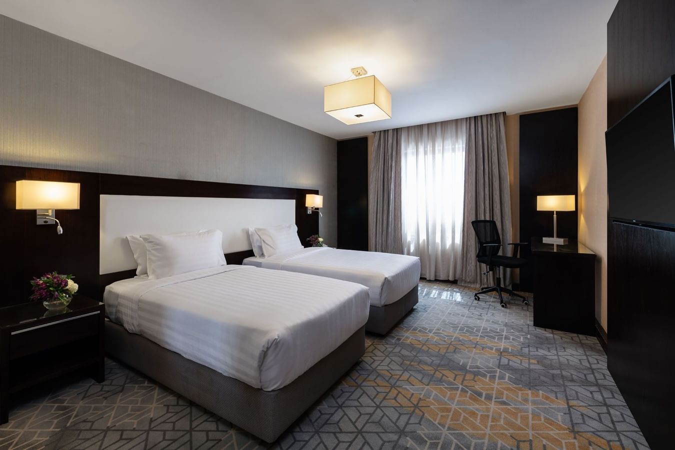 Nightstands and a work desk by the cozy beds in the Executive Two-Bedroom Suite with carpeted floors at Warwick Hotel Jeddah