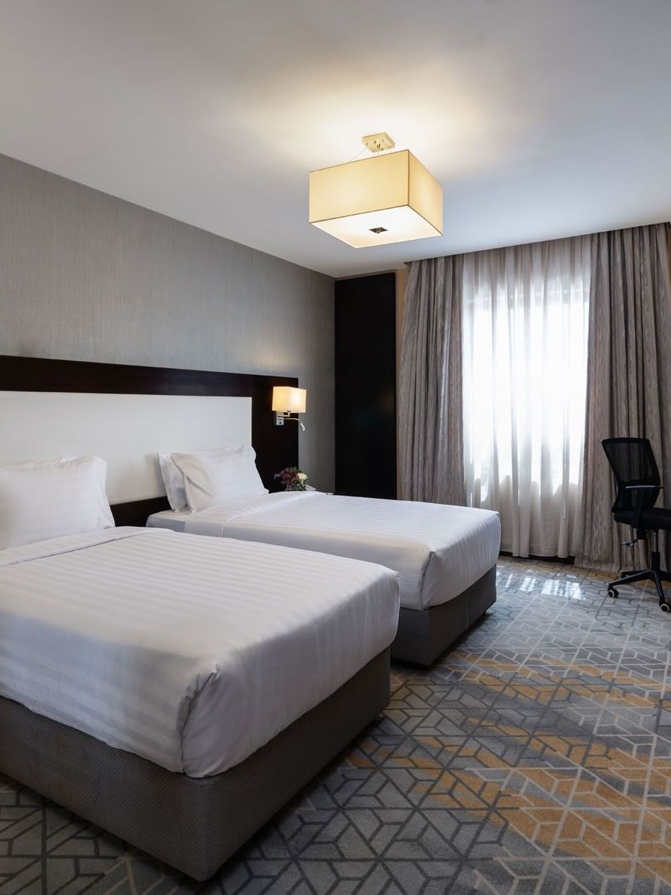 Nightstands and a work desk by the cozy beds in the Executive Two-Bedroom Suite with carpeted floors at Warwick Hotel Jeddah