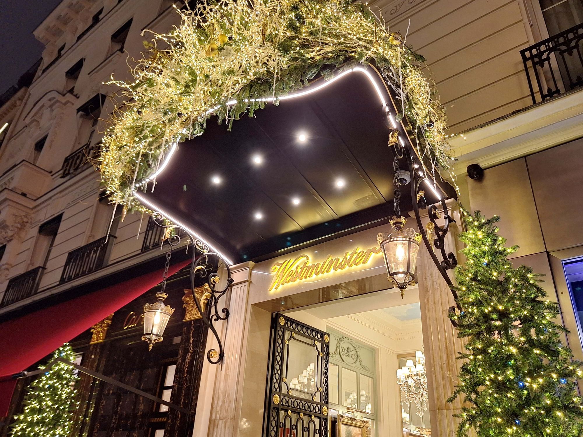 Festively decorated Hôtel Westminster - Paris entrance with greenery, twinkling lights, and a sign at night