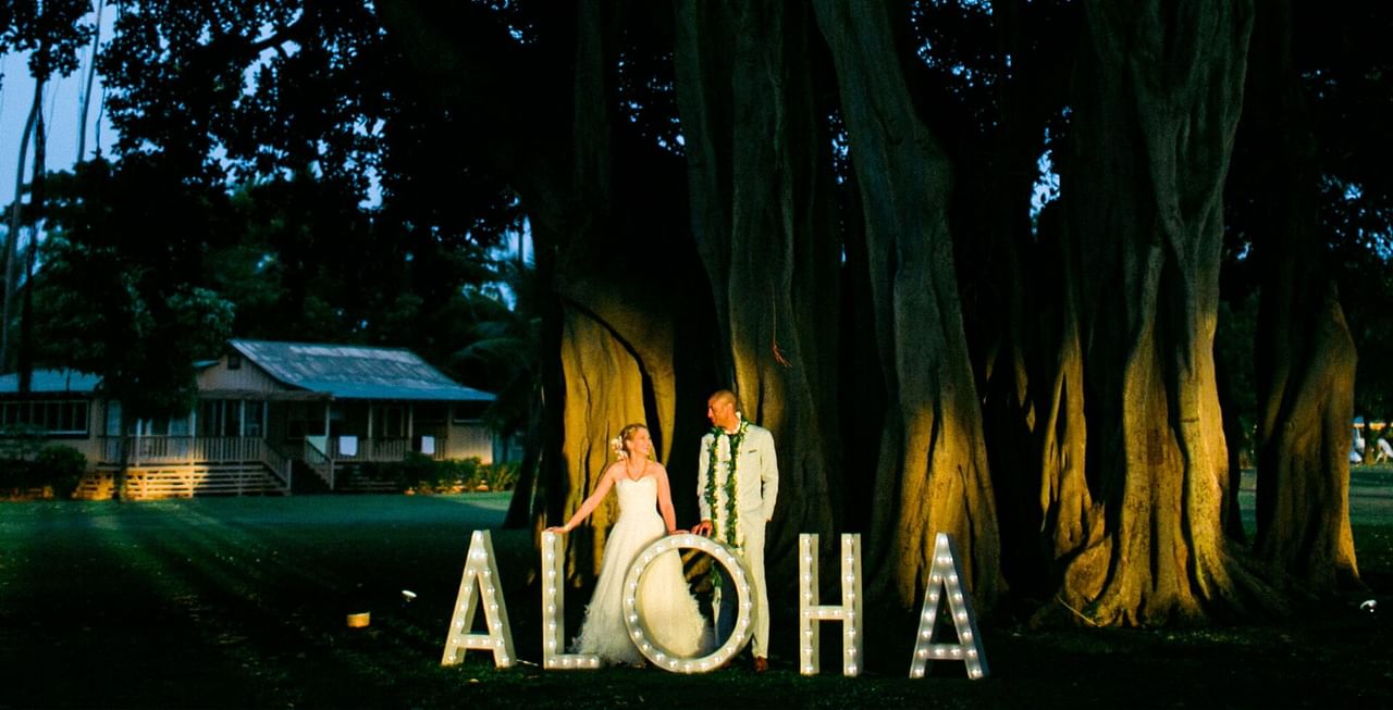 Bride and groom behind an Aloha sign