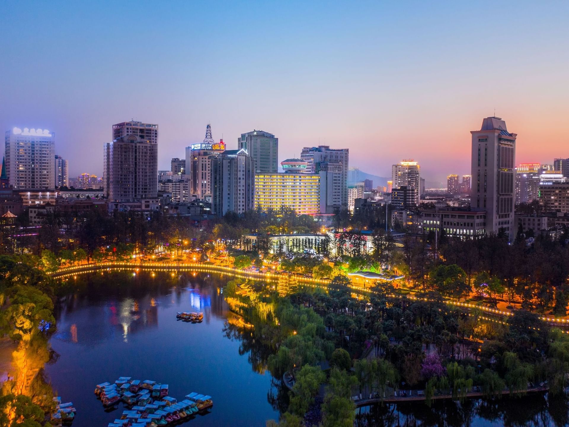 Twilight cityscape with buildings and a lake with boats near Park Hotel Group