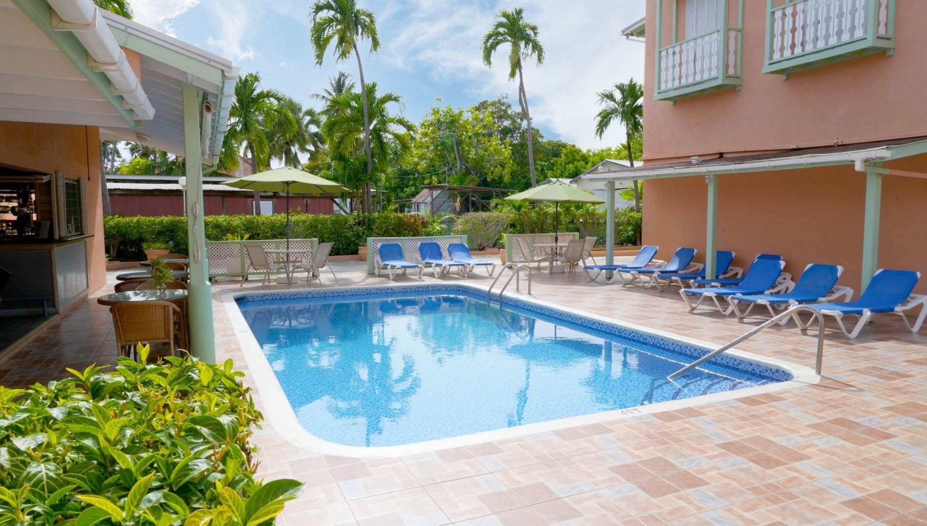 Bright outdoor swimming pool beside blue lounge chairs and green umbrellas with palm trees at Worthing Court Apartment