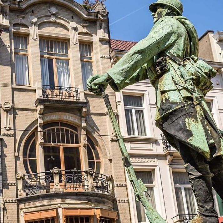 War Memorial statue by an Art Nouveau building with large circular windows near Hotel Barsey by Warwick