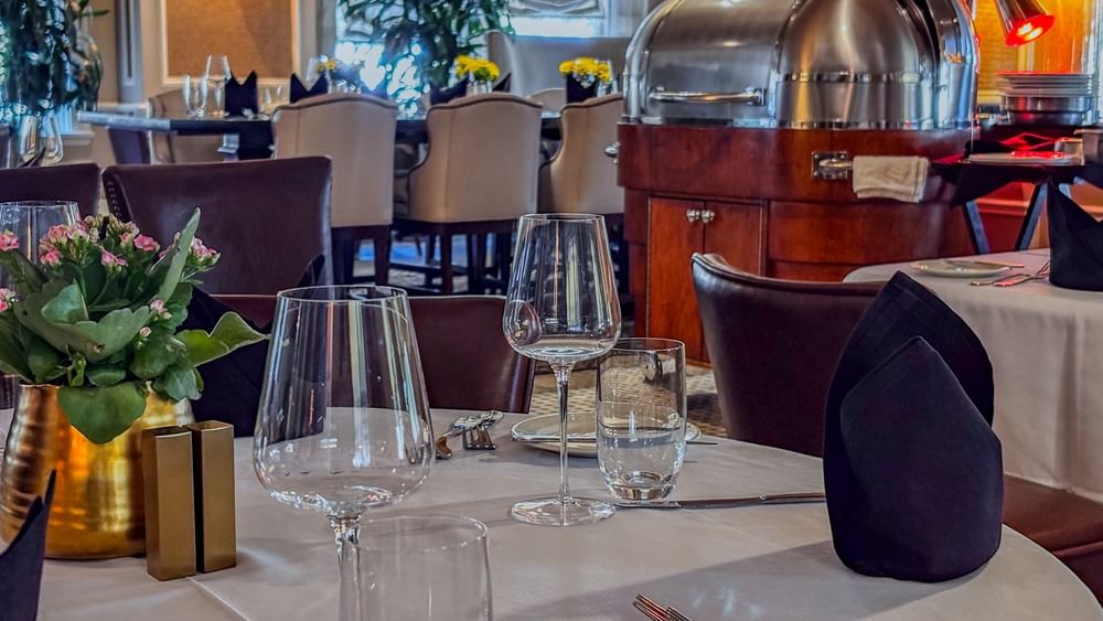 Wine glasses on a white table by a silver buffet under warm lights in The Landmark Prime Rib at Warwick Melrose Dallas