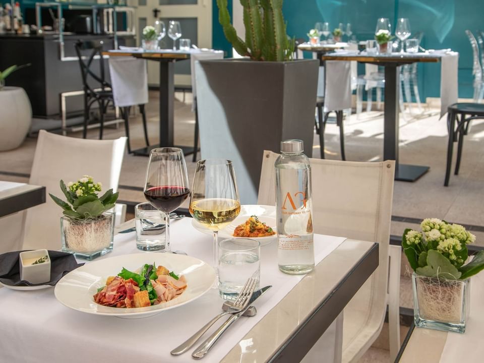 The Guardian Dehors dining table with a fresh salad, wine glasses, water bottle, and potted plants at The Guardian Hotel