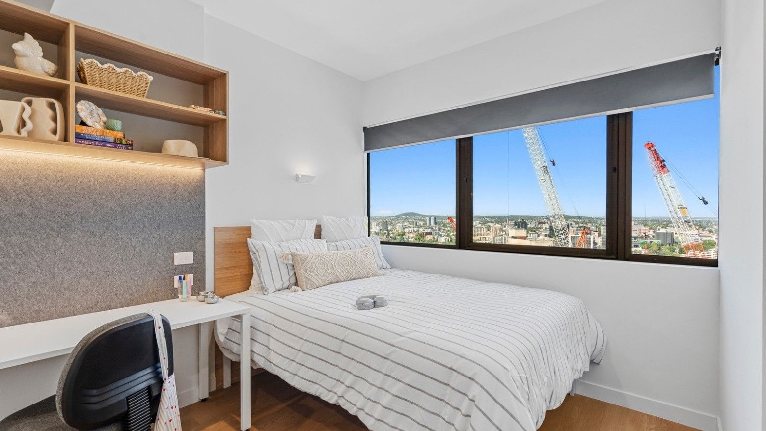 A cozy bedroom with a bed, desk, chair, and large windows at UniLodge Brisbane City.