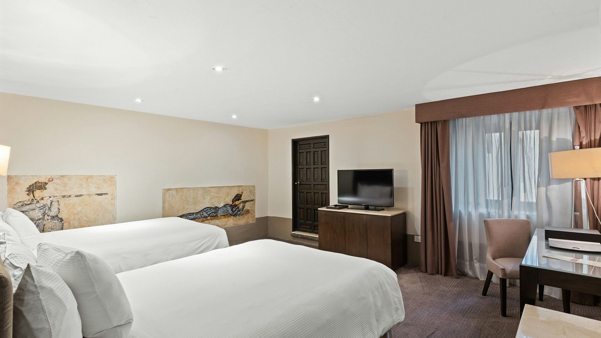 Two white beds in Double Grand Class Suite with a mural on the wall and a dark wood media console at Quinta Real Puebla
