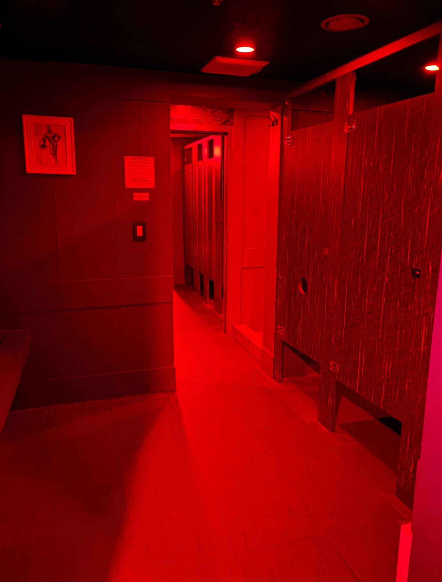 A dimly lit sauna area with red lighting, wooden walls and benches.