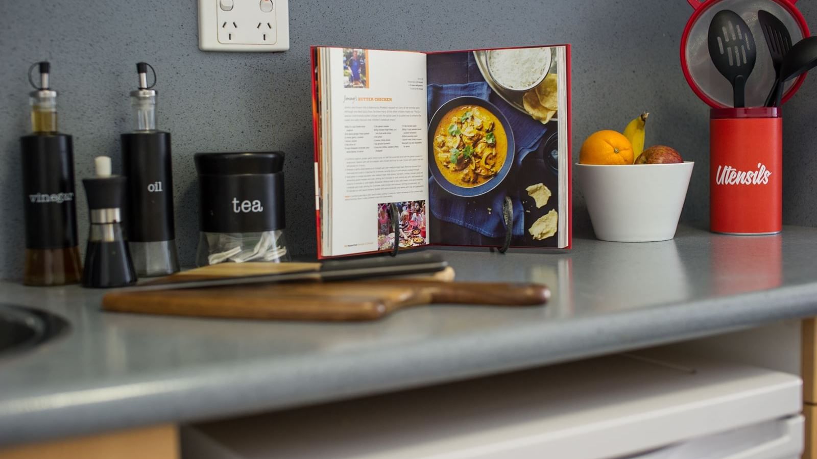 Modern kitchen counter with cookbook, condiment containers, fresh fruit bowl, and utensil holder at StudentLiving - on Margaret