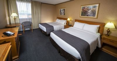 Two queen beds with a striped chair by a window, nightstands with lamps in Premier Tower at Glenmore Inn & Convention Centre