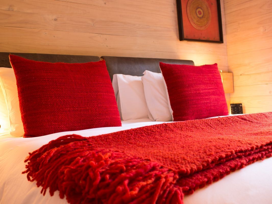 Deluxe Room com cama king, roupa de cama vermelha e paredes de madeira no NOI Puma Lodge em Machalí.