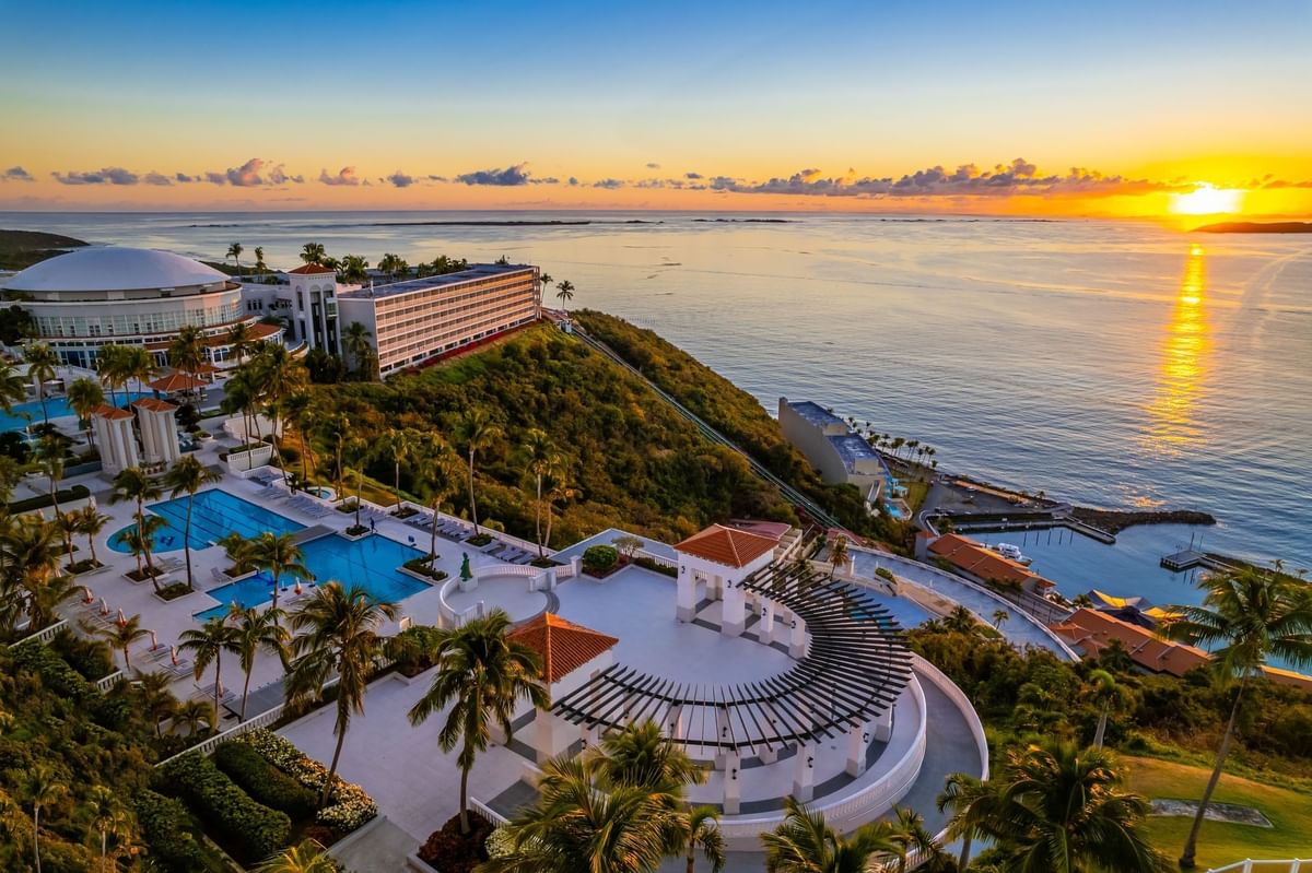 Aerial view of El Conquistador Resort with pools, palm trees, and Trellises Terrace, surrounded by lush greenery & the ocean