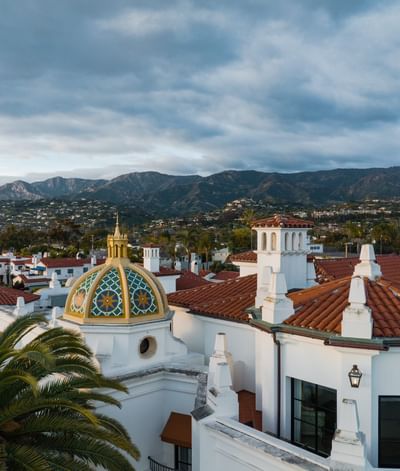 Drone view of the Santa Barbara Inn’s dome rooftops, nestled among palm trees, under a cloudy sky
