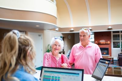 Elderly couple standing by a registration desk while interacting with a staff member at Rodd Brudenell River Resort
