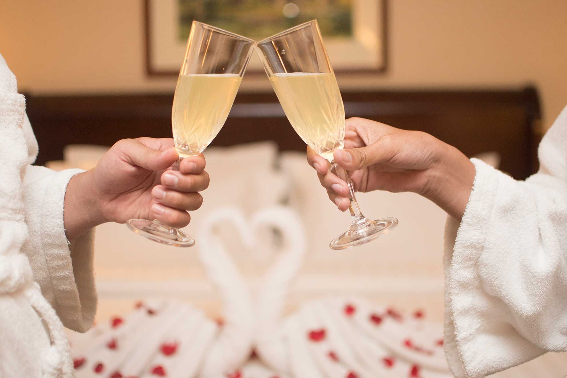 Close-up of a couple toasting champagne glasses on a bed with rose petals at Sunway Hotel Phnom Penh