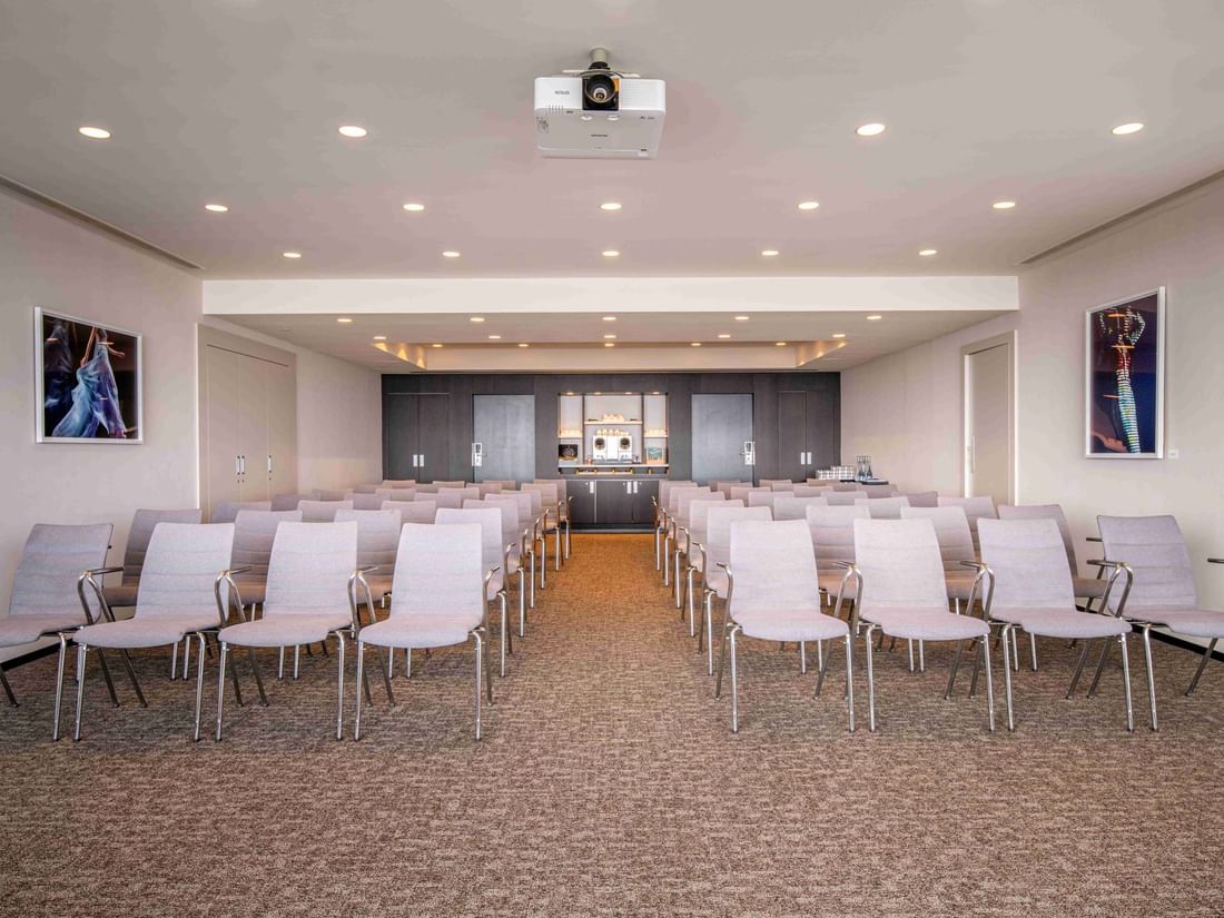 Meet 26 one meeting room with rows of chairs, a projector, and art on the walls at The Hotel Brussels