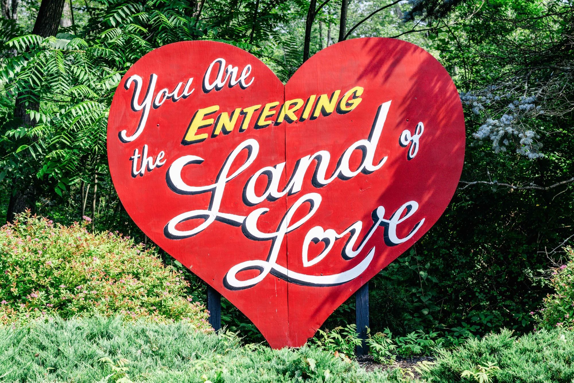 Red heart-shaped sign reading Land of Love in elegant script, surrounded by greenery at Cove Pocono Resorts