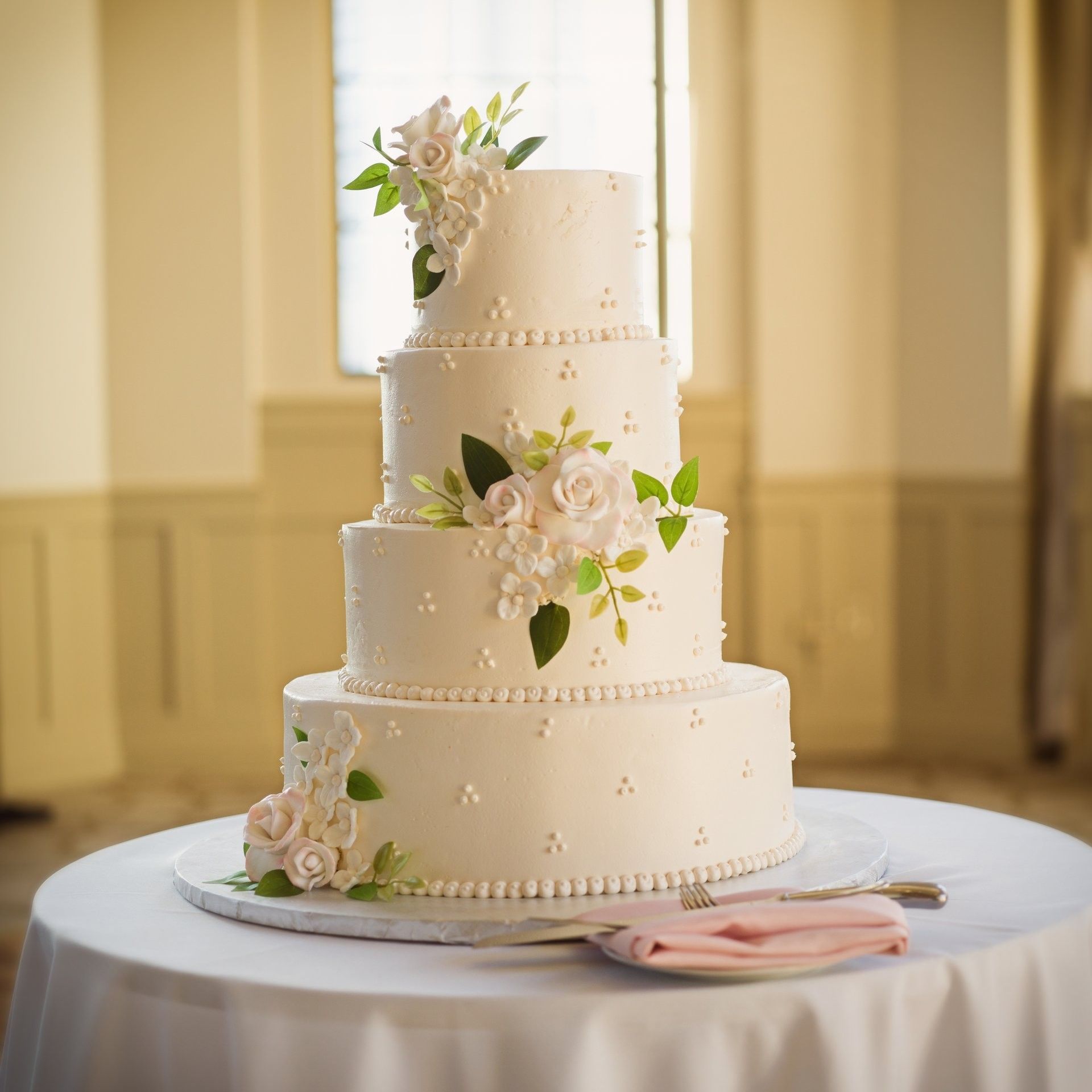 Four-tier wedding cake with roses and leaves on a table with a knife and napkin at Warwick Allerton Chicago