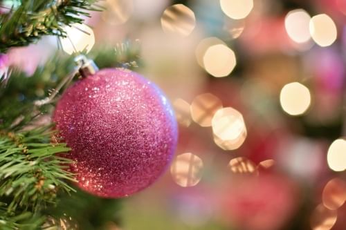 A close-up of a glittery pink ornament hanging on the branch of a Christmas tree. 