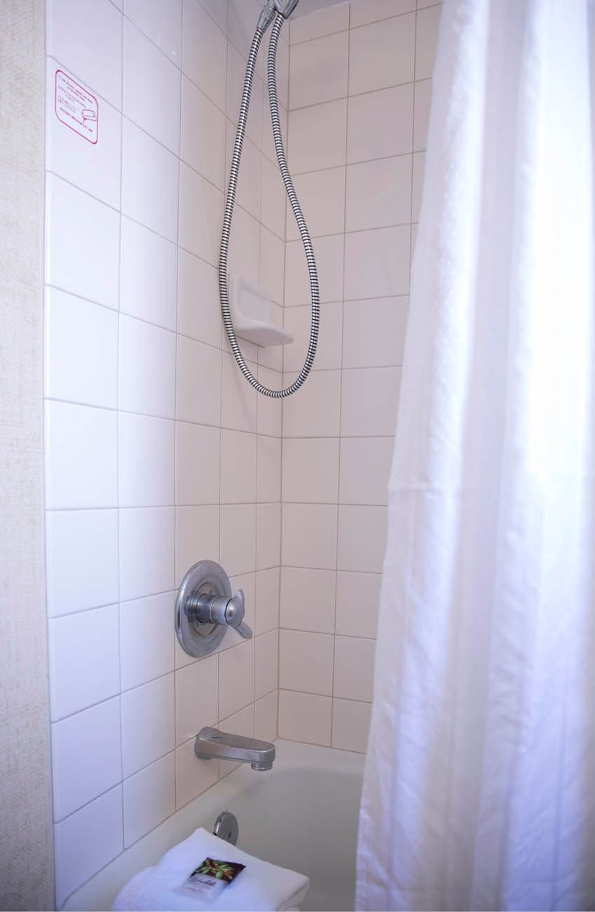 A bathroom with white tiles, a silver faucet, and a shower head above a bathtub with a white towel.