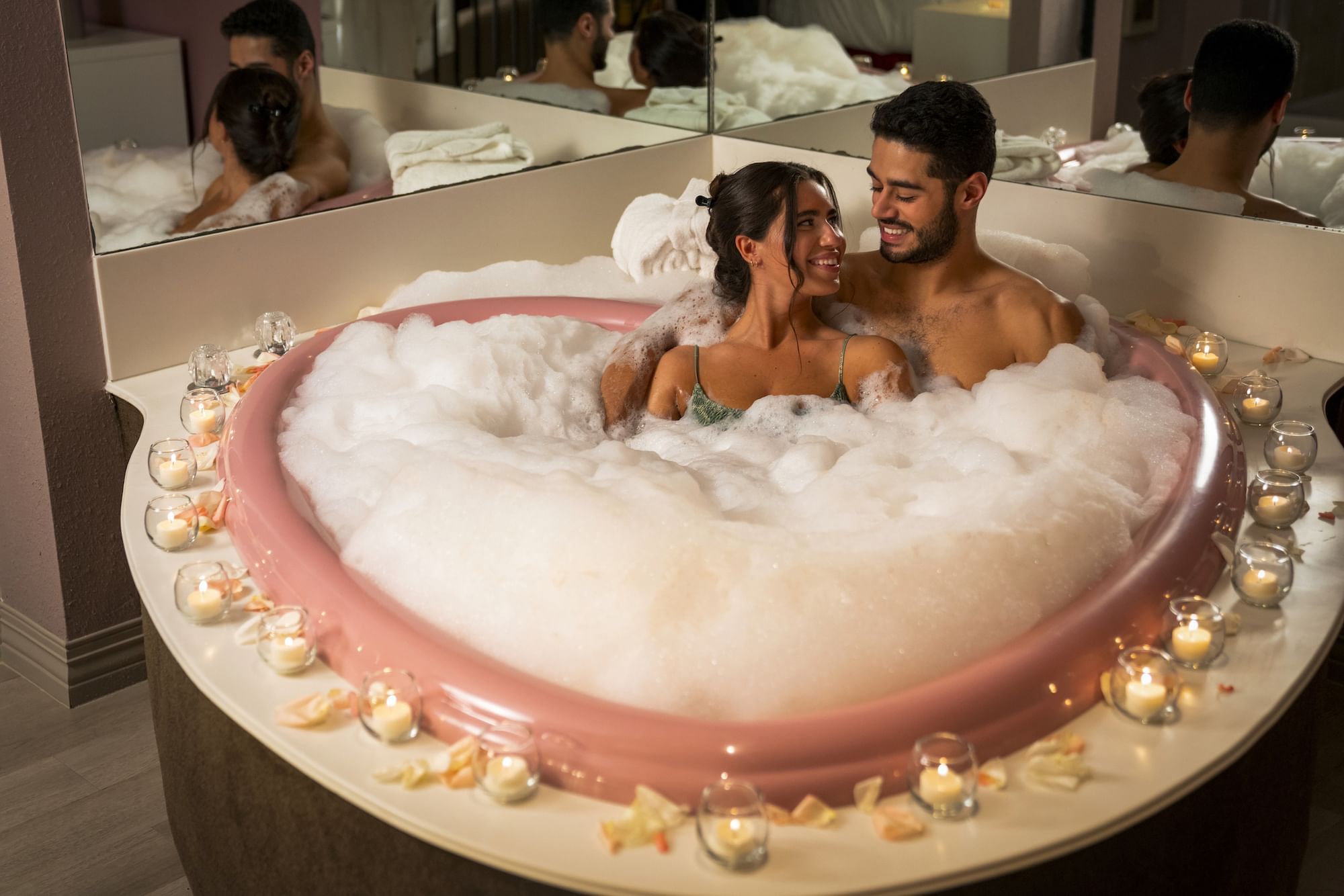 A couple relaxes in the Fairway Suite's bubble-filled heart-shaped tub, surrounded by candlelight at Cove Pocono Resorts