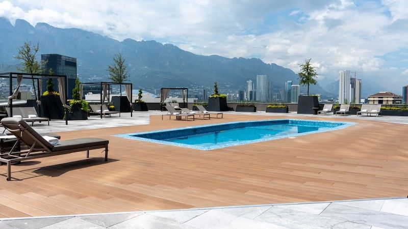 Lounge chairs by a wooden deck surrounding a blue pool under a mountain view at Camino Real Pedregal Mexico