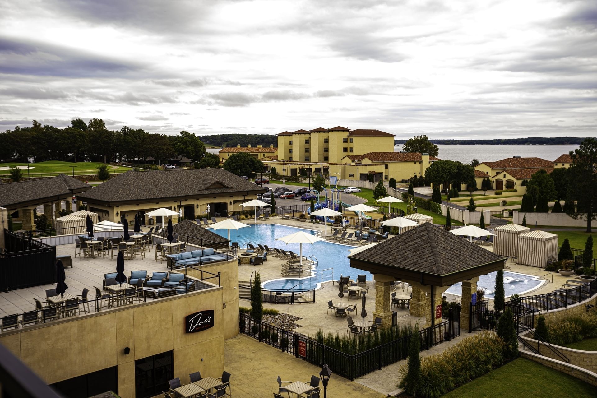 High-angle view of pool area with cabanas, tables, and a lake in the distance at Shangri-La Resort and Golf Club