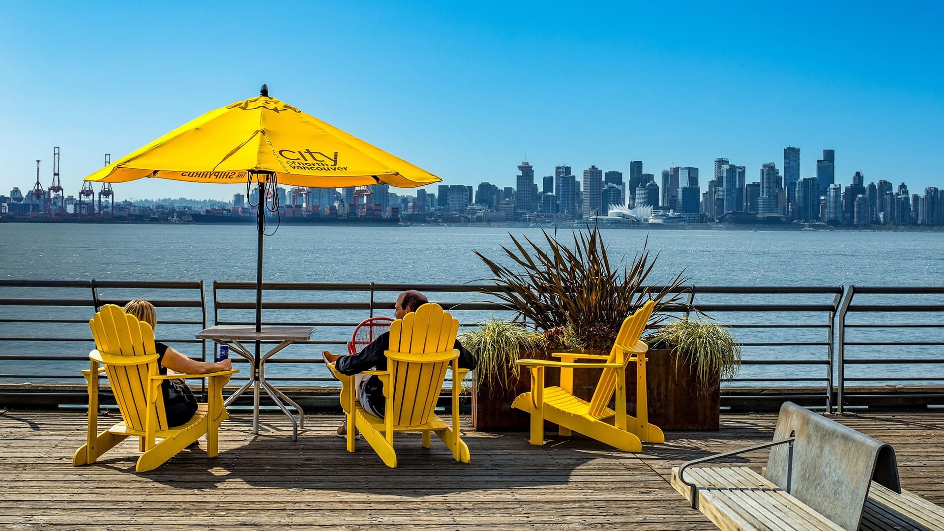 Waterfront deck with yellow chairs and a yellow umbrella at Coast Lonsdale Quay Hotel, overlooking the Vancouver skyline