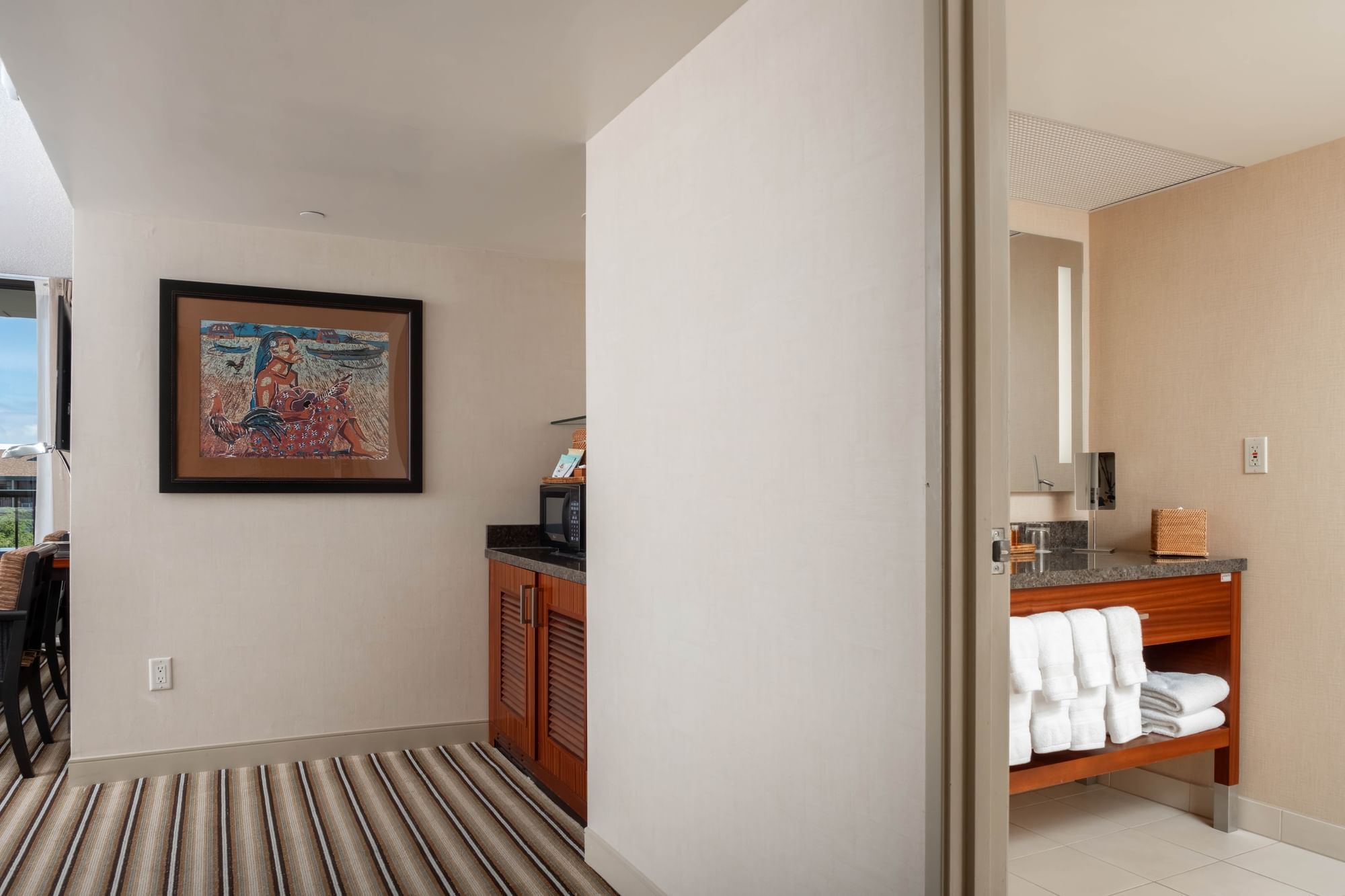 A hotel room with a kitchenette, bathroom, and queen bed