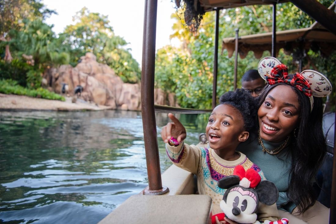 A woman in Minnie Ears with a child on her lap pointing into the distance as they enjoy a peaceful boat ride. 