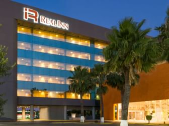 Modern exterior of Real Inn Nuevo Laredo at dusk, showing illuminated windows and tropical palm trees