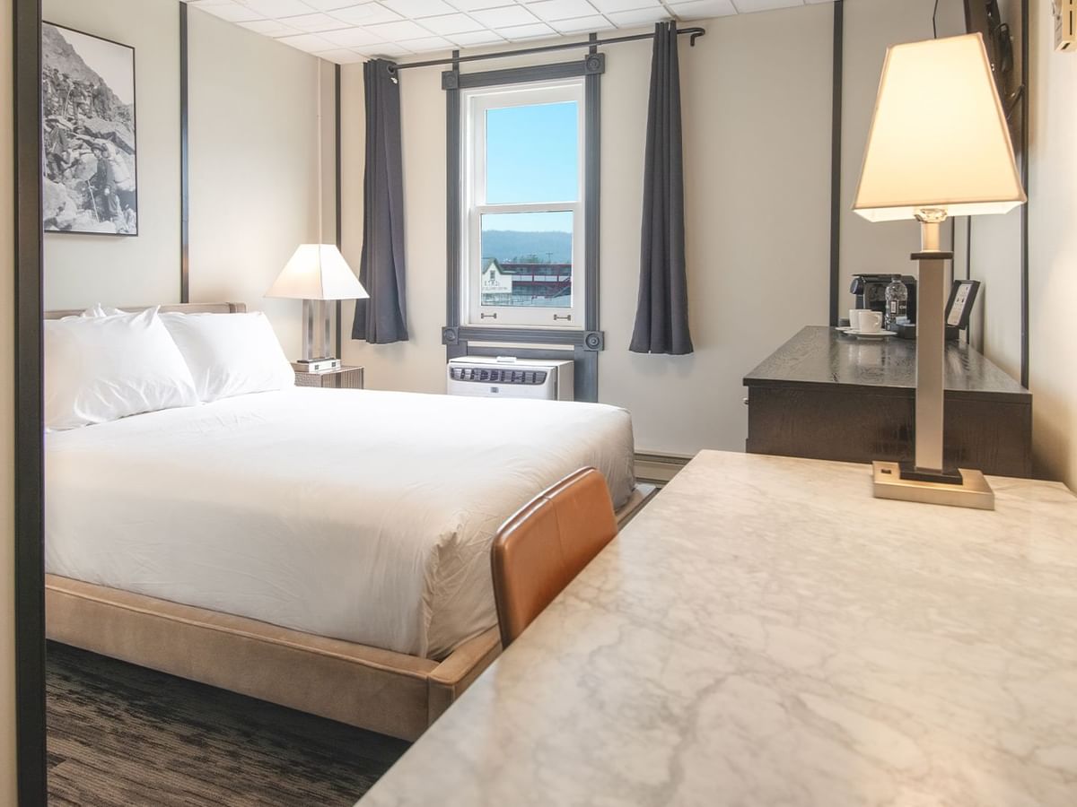 Hotel room with queen bed, night stand, lamp, coffee, and window