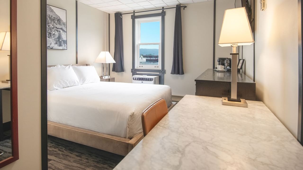 Hotel room with queen bed, night stand, lamp, coffee, and window