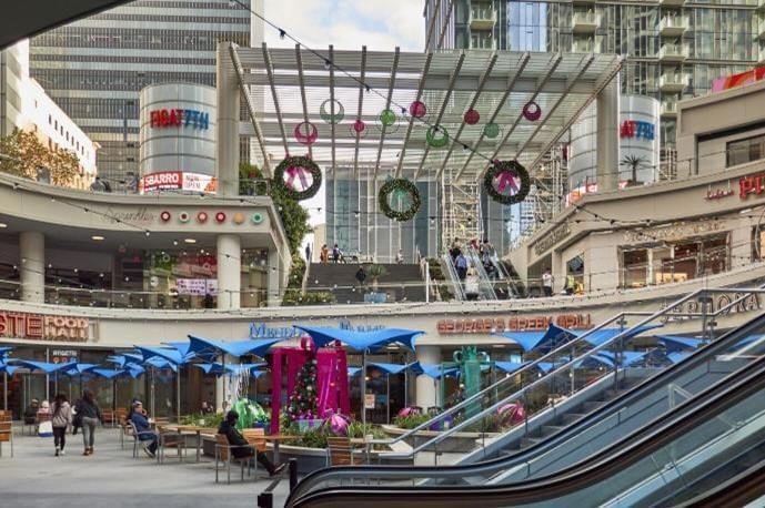 A outdoor shopping center with an escalator, seating area, and umbrella.