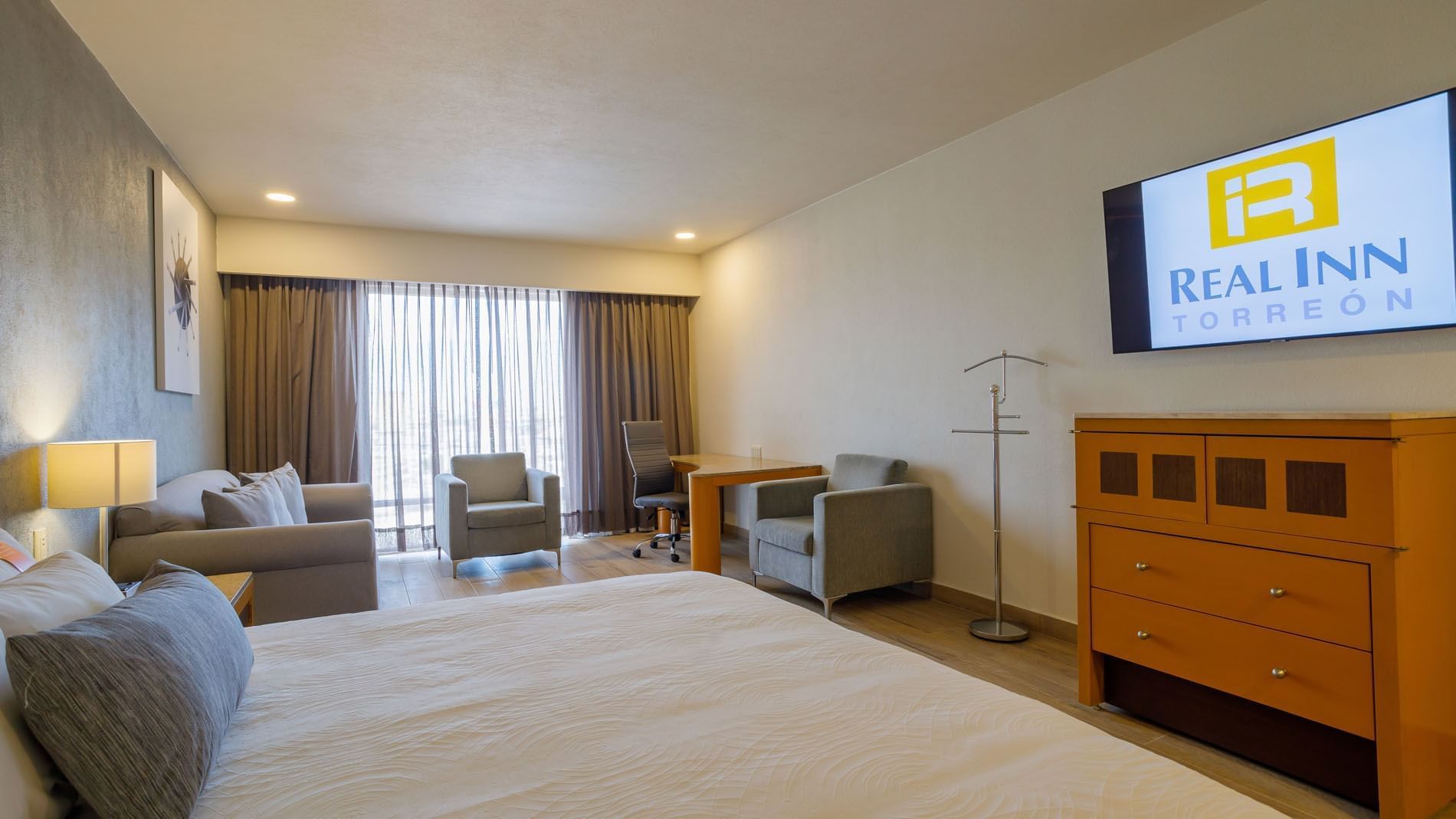King Junior Suite with a grey armchair, work area, and large windows for natural lighting at Real Inn Torreon