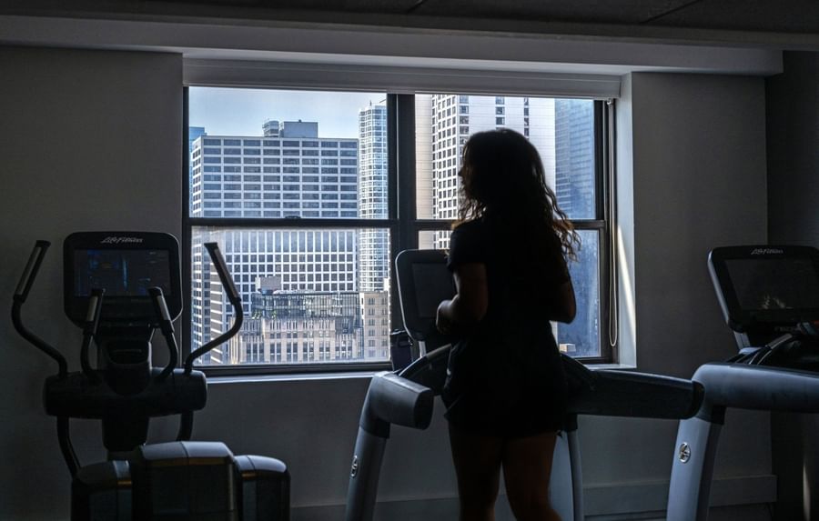 Guest running on a treadmill by a large window with a city view in Fitness Centre at Warwick Allerton Chicago