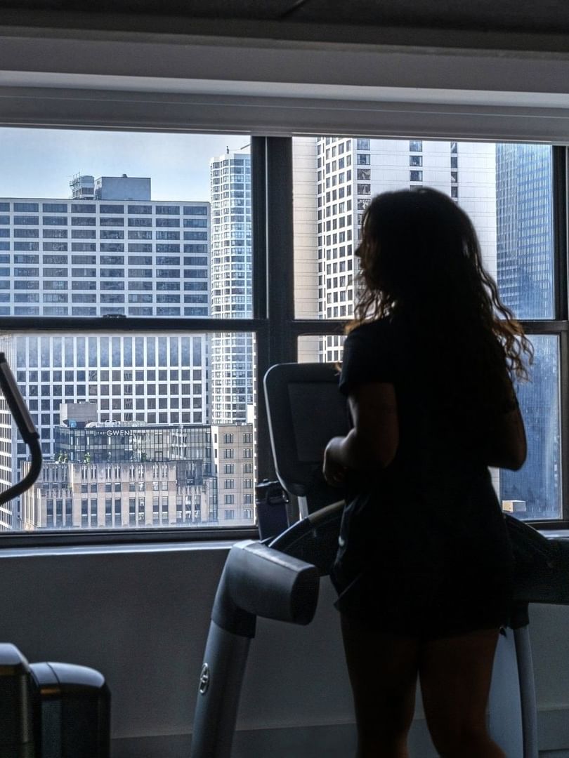 Guest running on a treadmill by a large window with a city view in Fitness Centre at Warwick Allerton Chicago