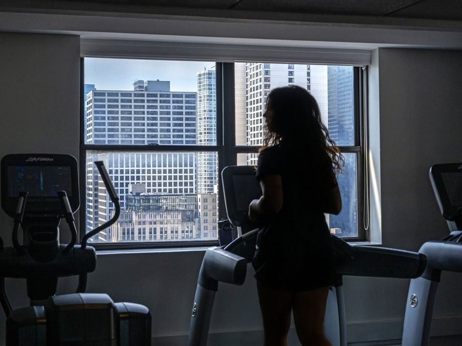 Guest running on a treadmill by a large window with a city view in Fitness Centre at Warwick Allerton Chicago