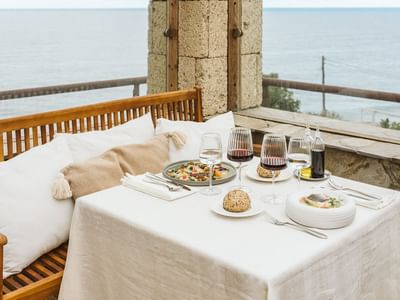A seaside dining setup with a table, food, wine, and ocean view.
