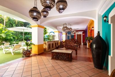 Lobby colorido con arcos, lámparas colgantes decorativas, muebles de madera tallada y vista al jardín en Los Arcos Suites