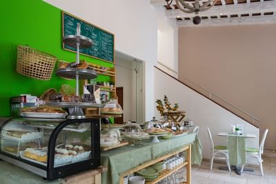 Corner café with rustic shelves, pastry display, green walls, and dining space at Billini Hotel Historic Luxury