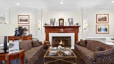 Two patterned couches facing a coffee table in front of a fireplace in the cozy lobby lounge at Avon Old Farms Hotel