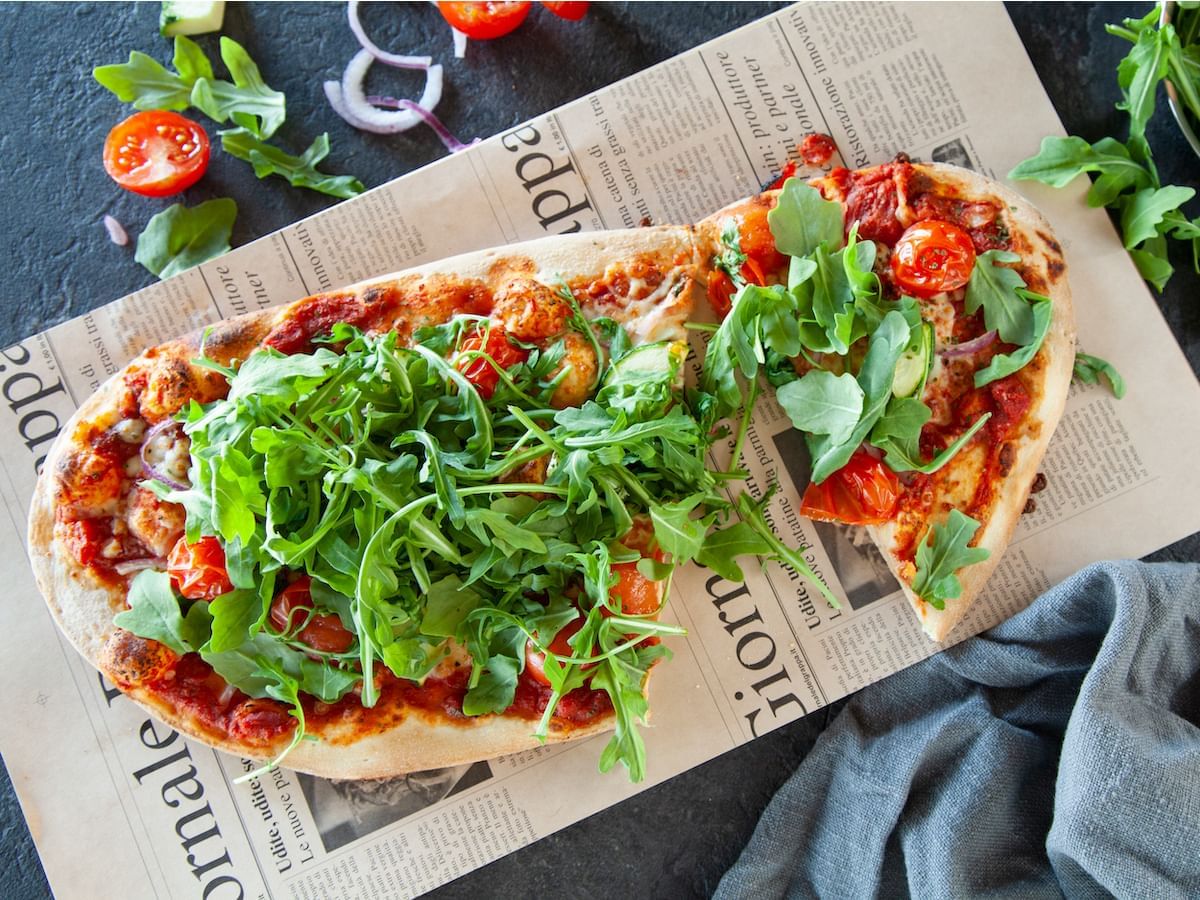 Pizza topped with arugula and tomatoes served in a restaurant at Acclaim Hotel Calgary