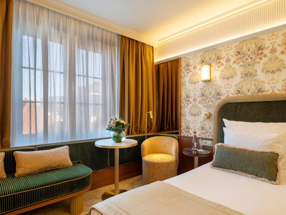 Superior Room with a green sofa by the window, round table and bed beneath floral wallpaper at Warwick Brussels Grand-Place