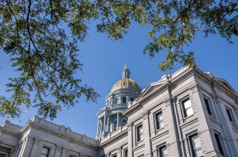 Gold dome by a grey stone building under a blue sky surrounded by green trees near at Warwick Denver