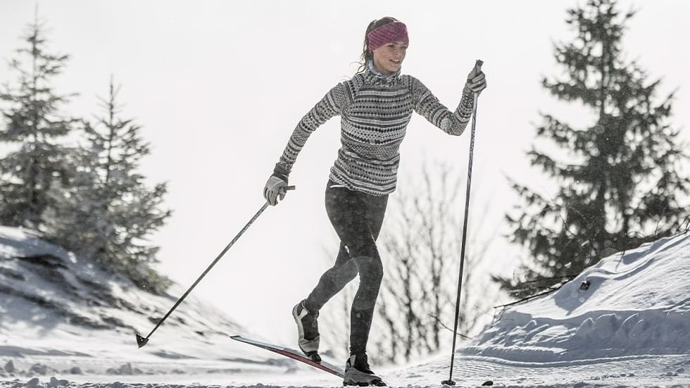 Woman cross-country skiing across a snow-covered field with pine trees near Falkensteiner Hotel Schladming