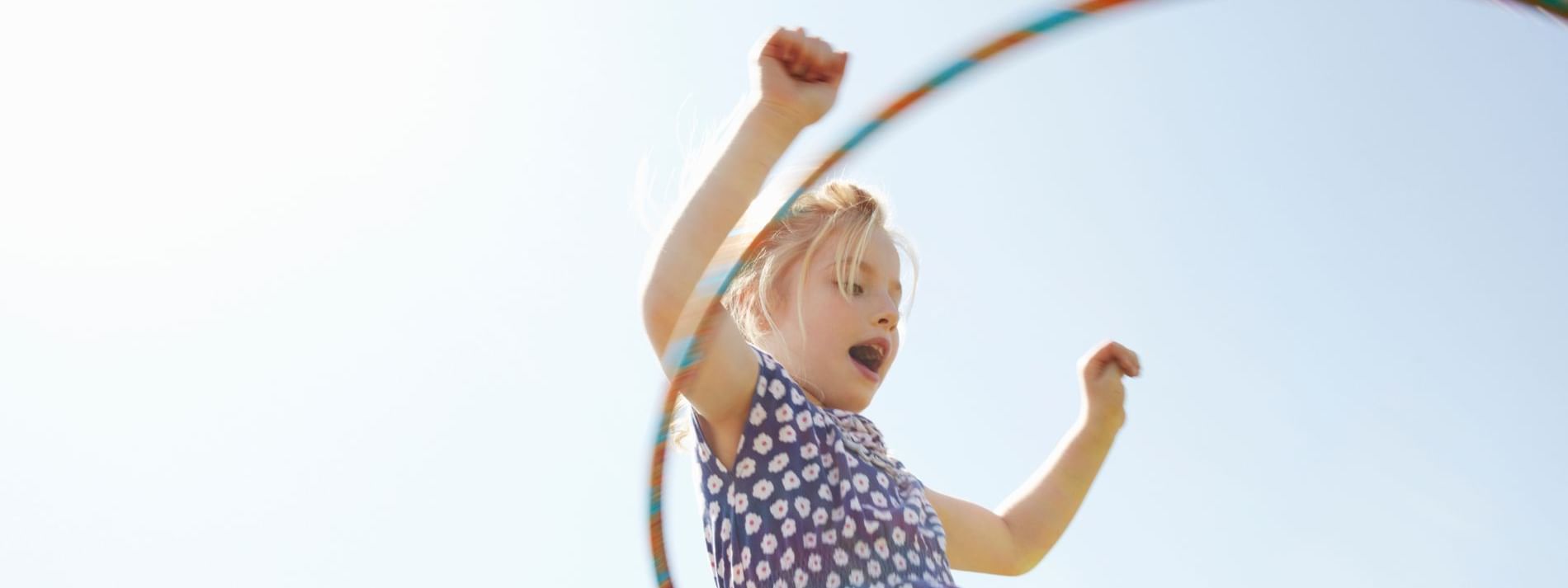 Young girl happily hula-hooping outdoors with arms raised at Novotel Sydney International Airport