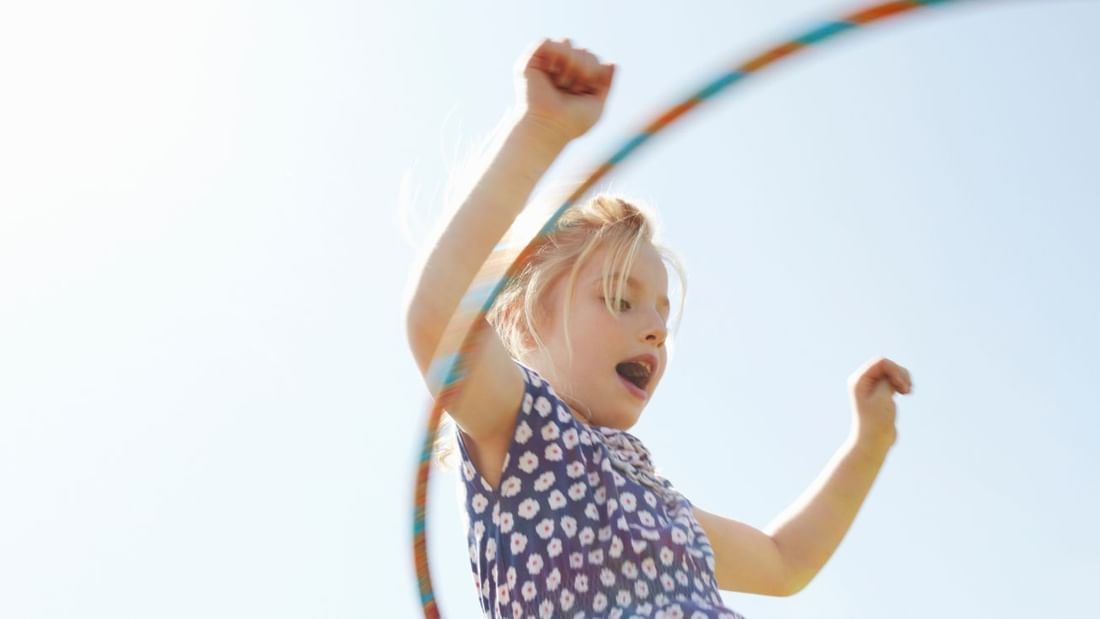 Young girl happily hula-hooping outdoors with arms raised at Novotel Sydney International Airport