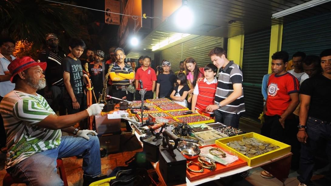 A group of people gathered around a street vendor's table with various items near Sunway Hotel Big Box