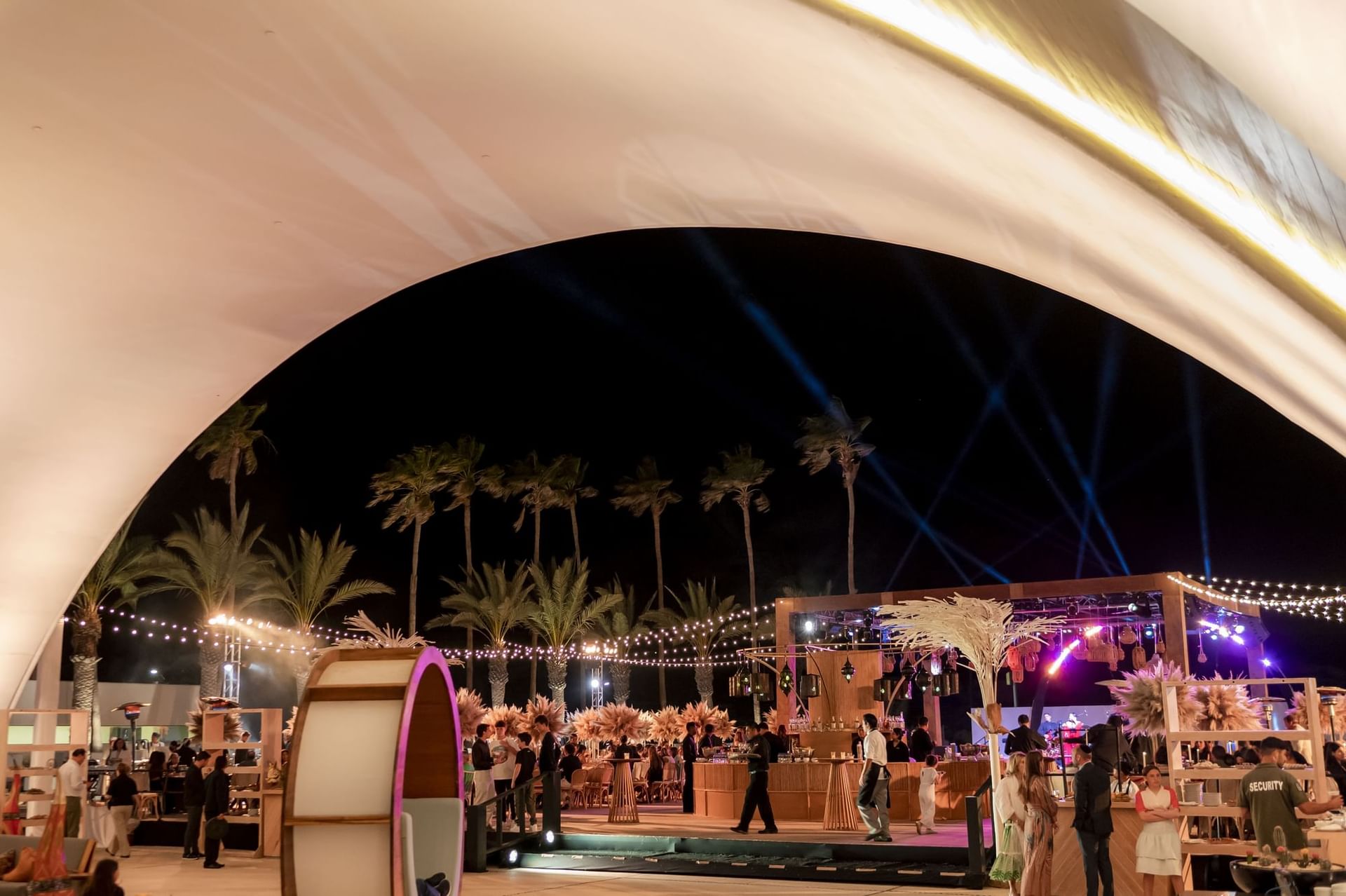 Nighttime gathering under a white tent with palm trees and a stage at Marquis Los Cabos Resort